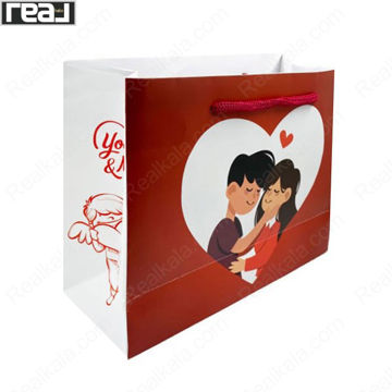 ساک دستی کادویی قرمز و سفید با طرح زوج عاشق داخل قلب، دارای بند قرمز و ابعاد 19 × 24.5 × 9.5 سانتی‌متر